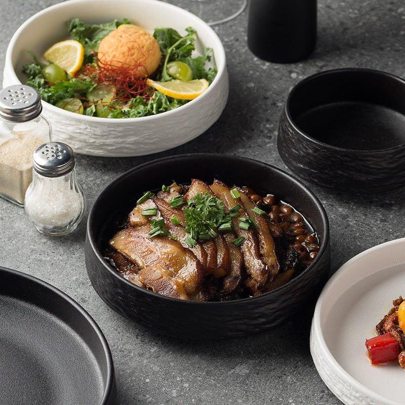 A set of Korean ceramic deep plates in black color, displayed with various dishes served on them.
