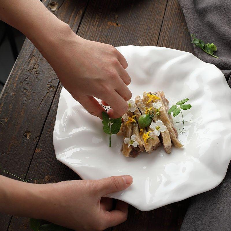 A white, irregularly shaped ceramic plate with food garnishes on it, placed on a wooden table.